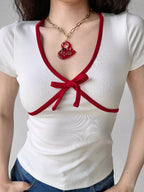 Full torso shot of a woman in a white top with red trim and a heart pendant necklace.