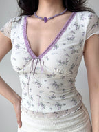 Woman in a white floral print top with purple lace trim and a white textured skirt, showing her side profile.
