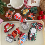 Assortment of holiday-themed hair claw clips displayed on a white tray and a wooden table, featuring gingerbread men, Santas, and snowmen.