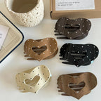 A variety of heart-shaped hair claw clips in different shades of brown, black, and cream, all decorated with a white polka dot pattern.