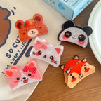 A flat lay of various cute animal-shaped hair clips including a bear, panda, cat, corgi, and fox, arranged on a white cloth and wooden surface.