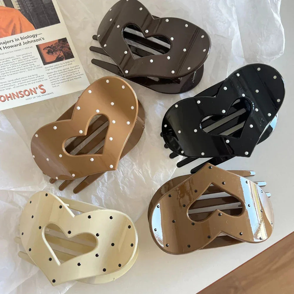 Assortment of five heart-shaped hair claw clips in black, cream, and brown, each adorned with white polka dots.