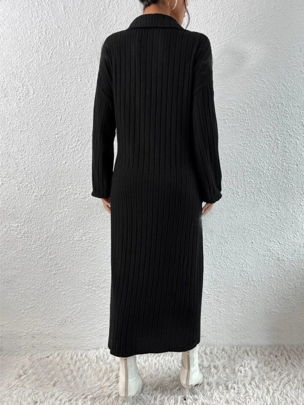 Back view of a woman wearing a black long-sleeved ribbed knit dress with a high slit and white boots.