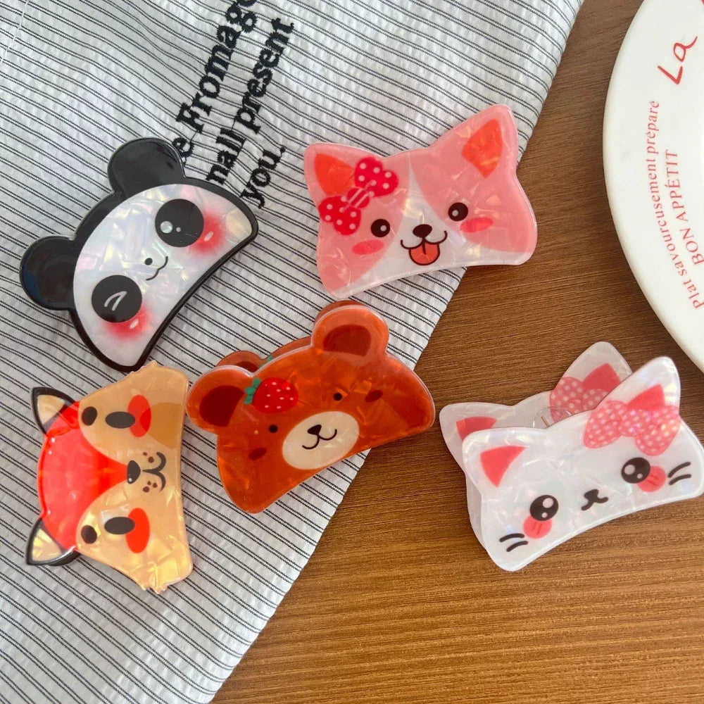 A group of charming animal hair clips, featuring a panda, corgi, bear, fox, and cat, presented on a striped cloth and wooden surface.