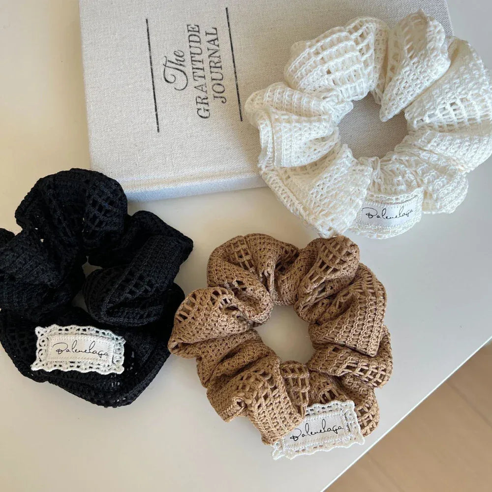 Three crocheted scrunchies in black, brown, and white arranged near a book