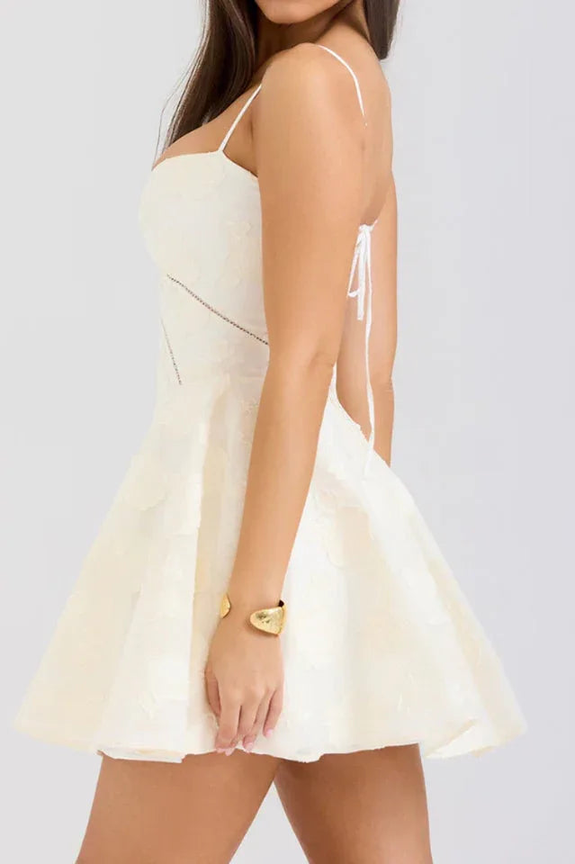 Side view of a woman in a cream-colored dress, highlighting the spaghetti straps and flared skirt.