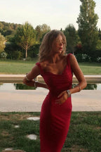 Woman wearing a red ruched dress outdoors with a pool in the background.
