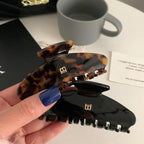 Hand holding two hair claw clips: black and tortoise shell, showcasing the 'B' logo