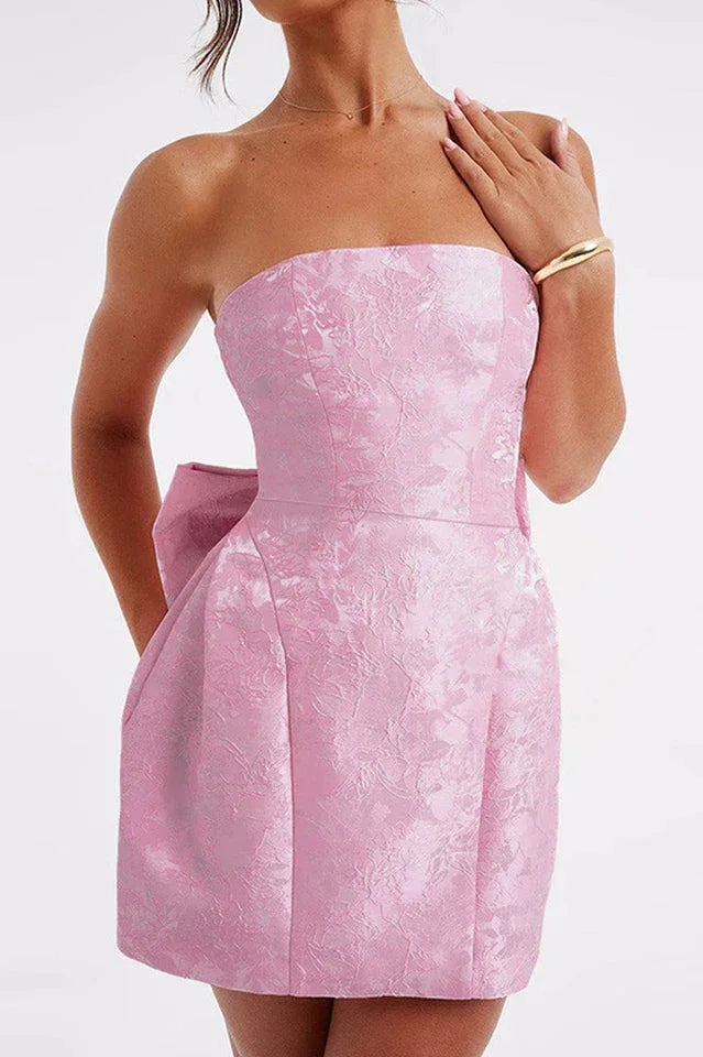 Front detail of a pink strapless dress with a textured fabric and a bow accent.