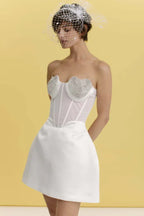 Close-up of a model wearing a white strapless dress with heart-shaped embellishments on the bust, a corset bodice, and a full skirt.