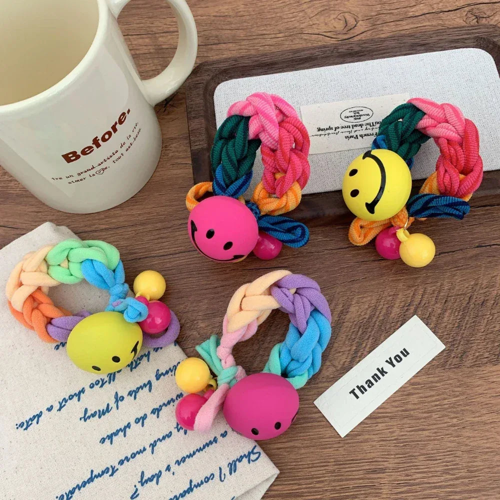 A collection of colorful braided hair ties with smiley face charms and beads, displayed with a mug and other items.