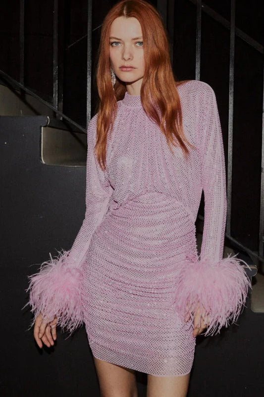 Woman with red hair wearing a pink sequined dress with feather trim on the sleeves.
