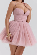 woman in pink mini dress with ruched bodice and tulle skirt, hand on chest