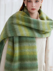 Close-up of a woman wearing a cream coat and a green striped scarf with fringe detail.