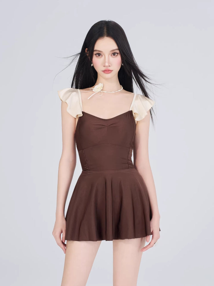 Woman wearing a brown and cream one-piece swimsuit with ruffled cap sleeves and a sweetheart neckline, shown from the front with a flared skirt.