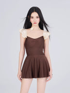 Woman wearing a brown and cream one-piece swimsuit with ruffled cap sleeves and a sweetheart neckline, shown from the front with a flared skirt.