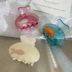 A trio of decorative hair clips in pink, blue, and cream, each containing a small fish.