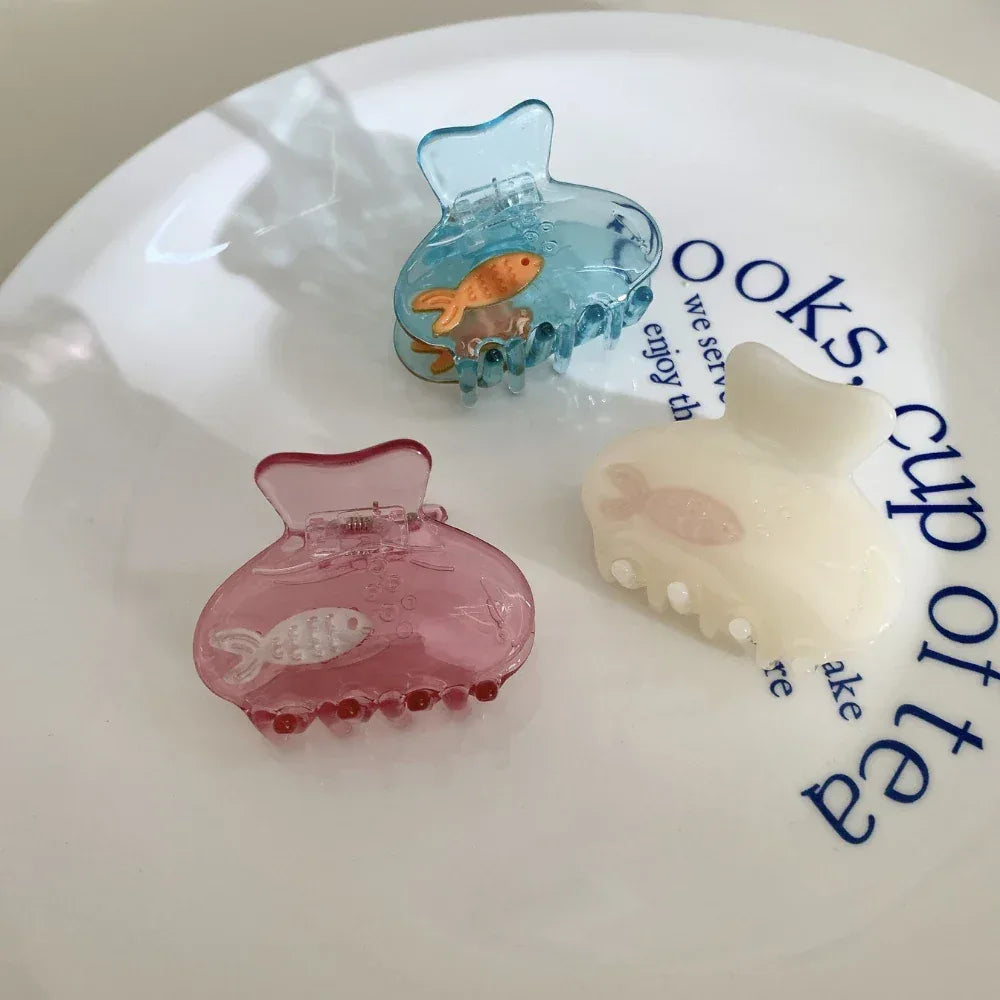 Assorted colorful hair claw clips with embedded fish designs, displayed on a white plate with text.