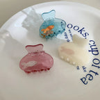 Assorted colorful hair claw clips with embedded fish designs, displayed on a white plate with text.
