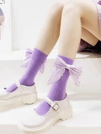 Close-up of purple ribbed socks with large, embellished bows around the calf area, worn with white Mary Jane shoes.