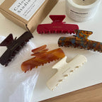 A top-down view of five hair claw clips in different colors, displayed on a white surface with some crumpled white paper.