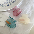 A collection of three fish-themed hair clips in blue, pink, and cream, scattered on white paper.