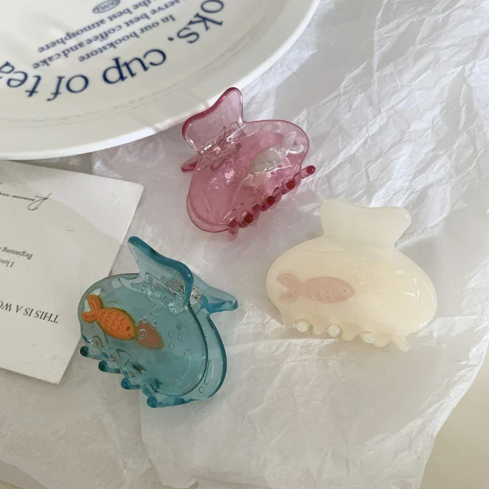 A collection of three fish-themed hair clips in blue, pink, and cream, scattered on white paper.