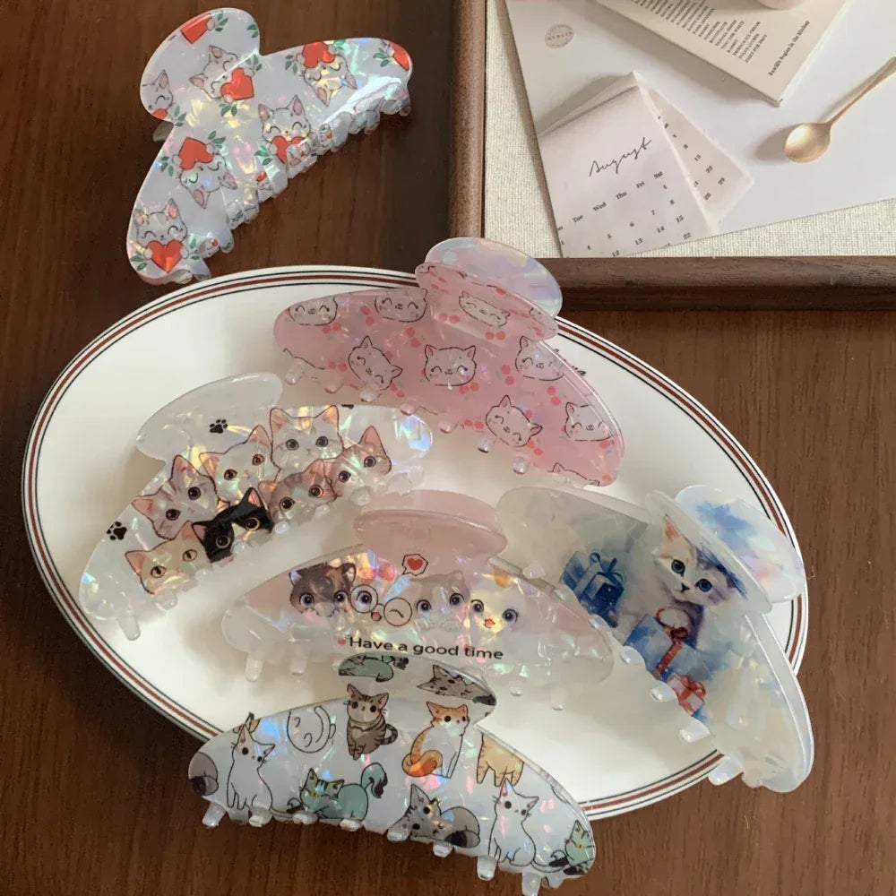 A selection of cat-themed claw clips laid out on a white plate and a wooden surface.
