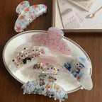 A selection of cat-themed claw clips laid out on a white plate and a wooden surface.