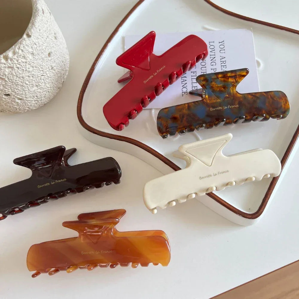 A collection of five hair claw clips in various colors, including red, tortoiseshell, dark brown, amber, and cream, arranged on a white surface.