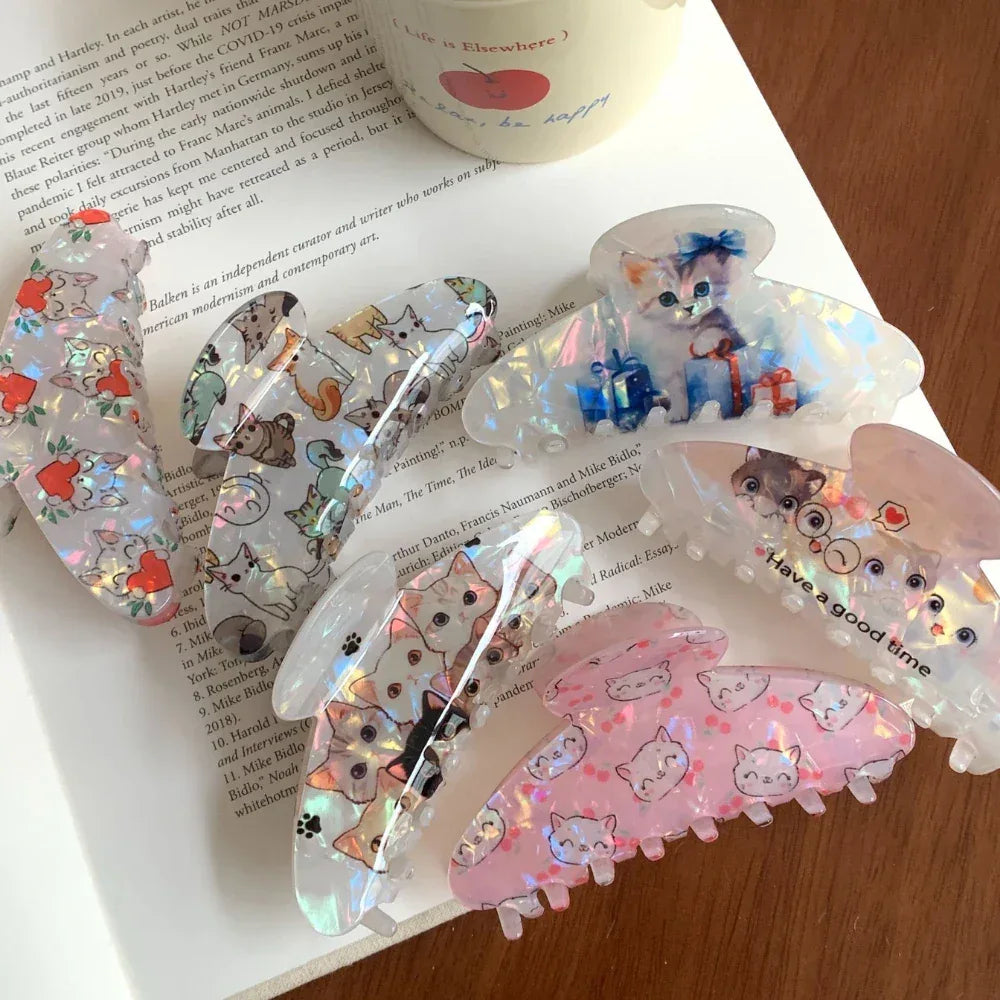 Overhead view of several cat-themed claw clips scattered on a book and a wooden surface.