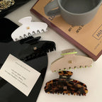 Overhead view of four hair claw clips: white, black, beige with neon green accents, and tortoise shell