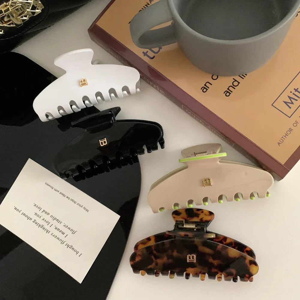 Overhead view of four hair claw clips: white, black, beige with neon green accents, and tortoise shell