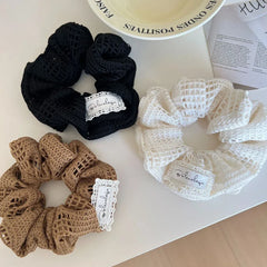 A collection of black, brown, and white crocheted scrunchies on a white table