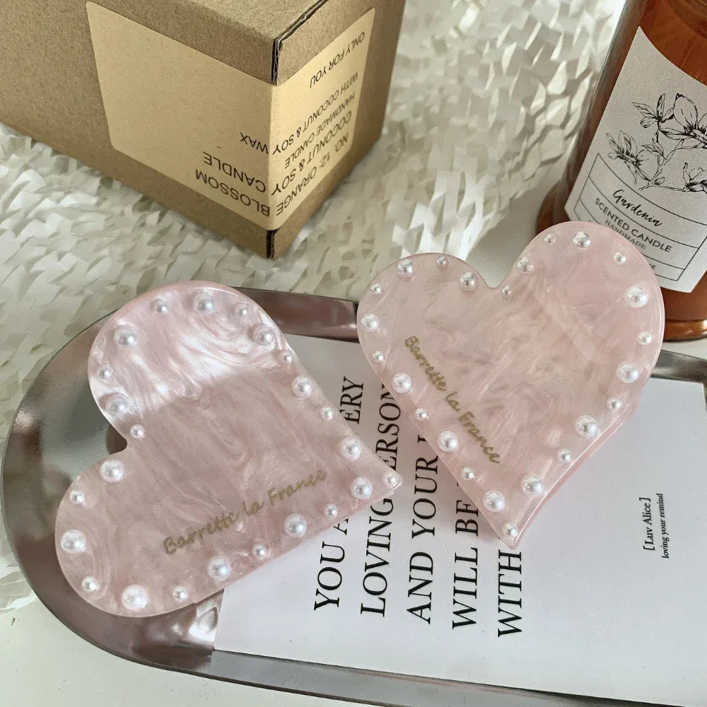 Two pink marbled heart-shaped hair clips with faux pearl embellishments, placed on a tray with printed text.