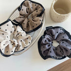 A metal basket containing two scrunchies with floral patterns, and a third scrunchie with a floral pattern placed beside it on a white surface.