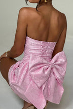 Model in a pink strapless dress with a large bow, posing.