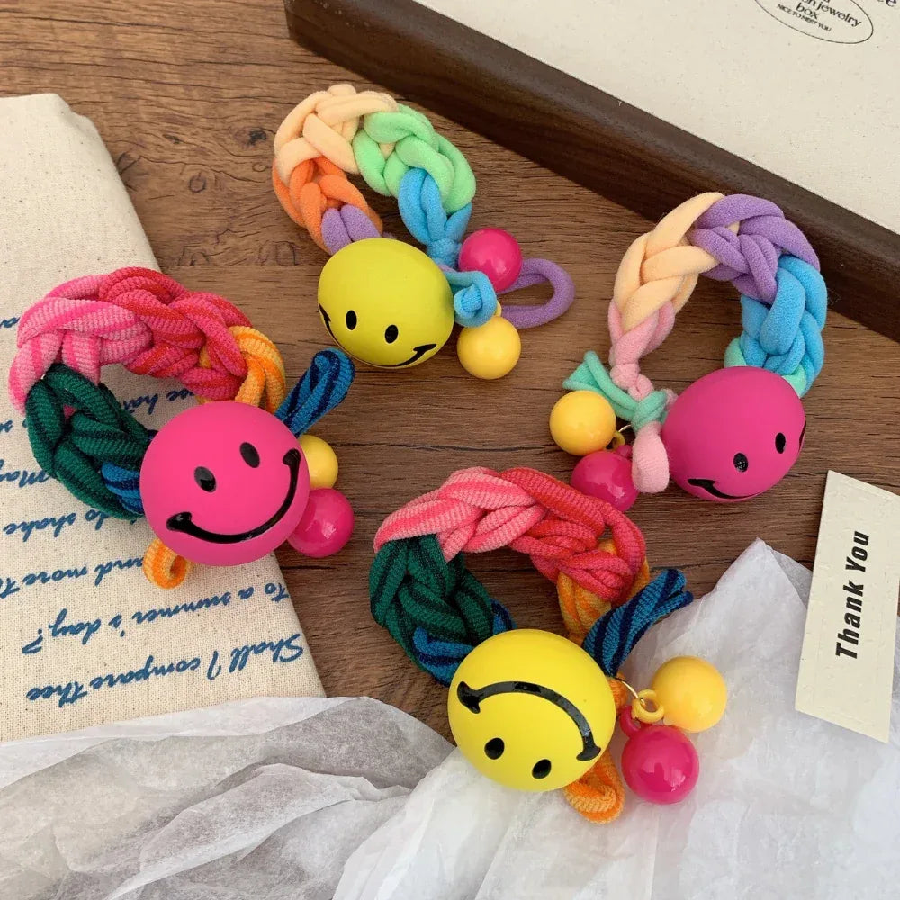 Several cheerful braided hair ties featuring smiley face charms and colorful beads, arranged on a wooden surface.