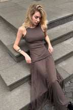Woman sitting on steps wearing a brown ruched maxi dress with a halter neckline.