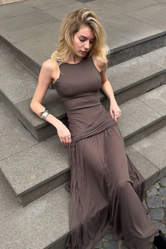 Woman sitting on steps wearing a brown ruched maxi dress with a halter neckline.