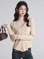 Woman wearing a beige ribbed knit cardigan with lace trim and a V-neck, holding a brown handbag.