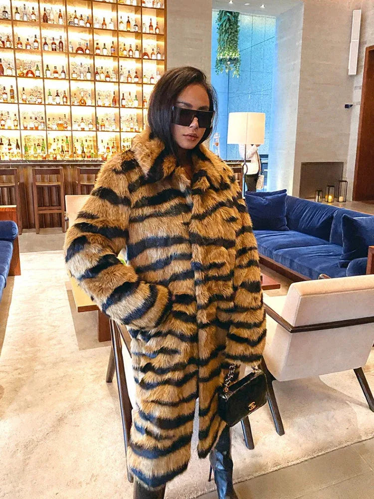 Woman in a faux fur tiger stripe coat and black boots, holding a black handbag, standing in a lounge area.