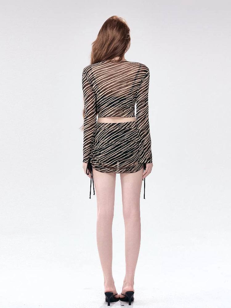 Back view of a woman in a long-sleeve sheer striped top and matching mini skirt.