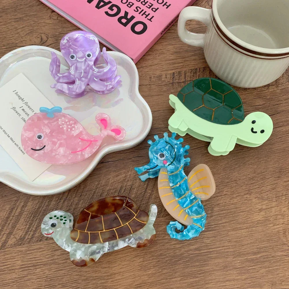 A collection of acrylic hair clips including a pink whale, a purple octopus, a blue seahorse, and two turtles of different colors.