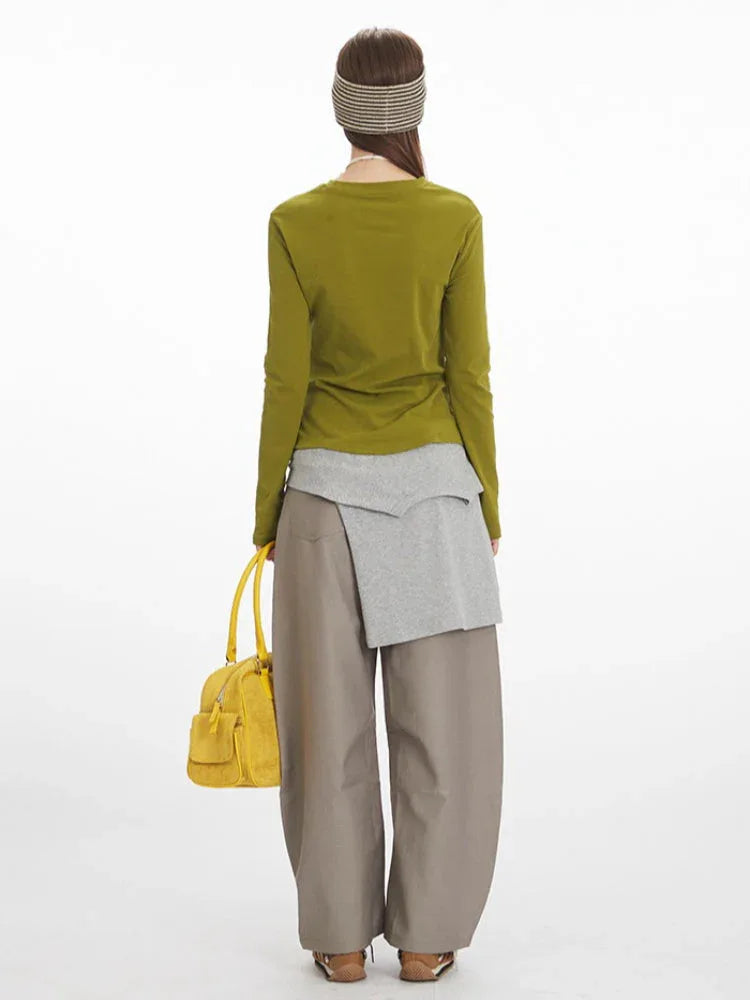Rear view of a woman wearing a green long-sleeved top, grey layered knit, and taupe wide-leg pants.