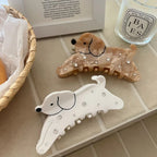 Close-up of two dog-shaped hair claw clips, one white and one brown, with sparkling embellishments, on a textured surface