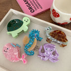 A tray filled with acrylic hair clips shaped like sea creatures: a pink whale, a purple octopus, a blue seahorse, and two turtles.