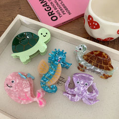 A tray filled with acrylic hair clips shaped like sea creatures: a pink whale, a purple octopus, a blue seahorse, and two turtles.