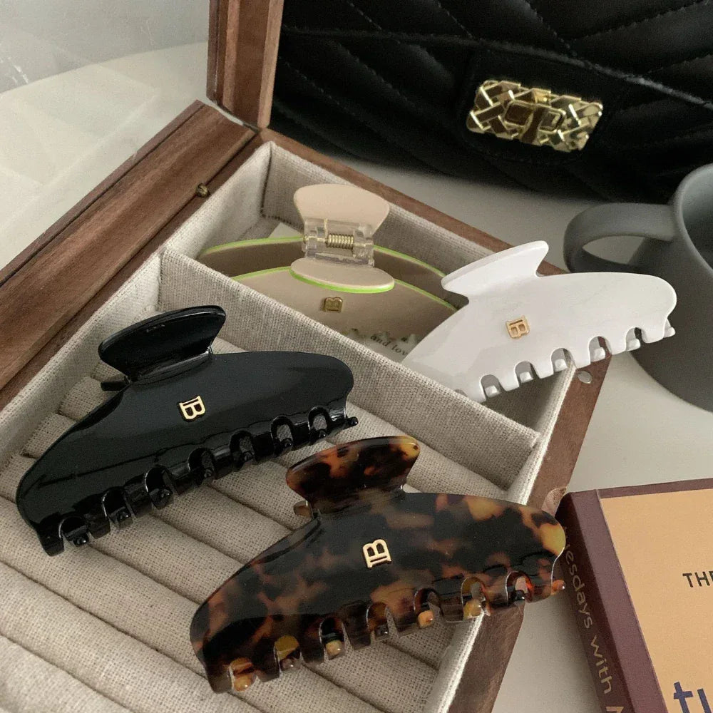 Collection of four hair claw clips in a wooden box: black, tortoise shell, beige with neon green accents, and white