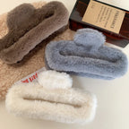 White, brown, and gray faux fur claw clips arranged with a bottle and a book